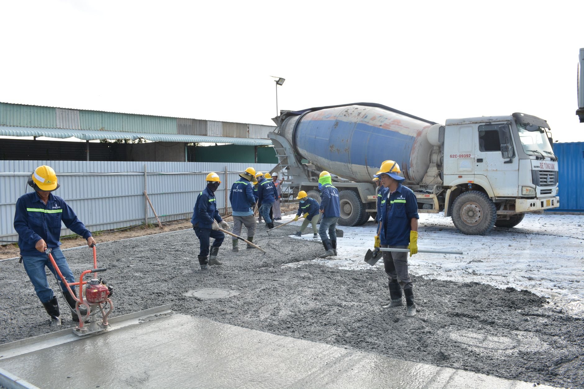 Workers in safety gear pouring concrete from a mixer truck, as for container corner footings
