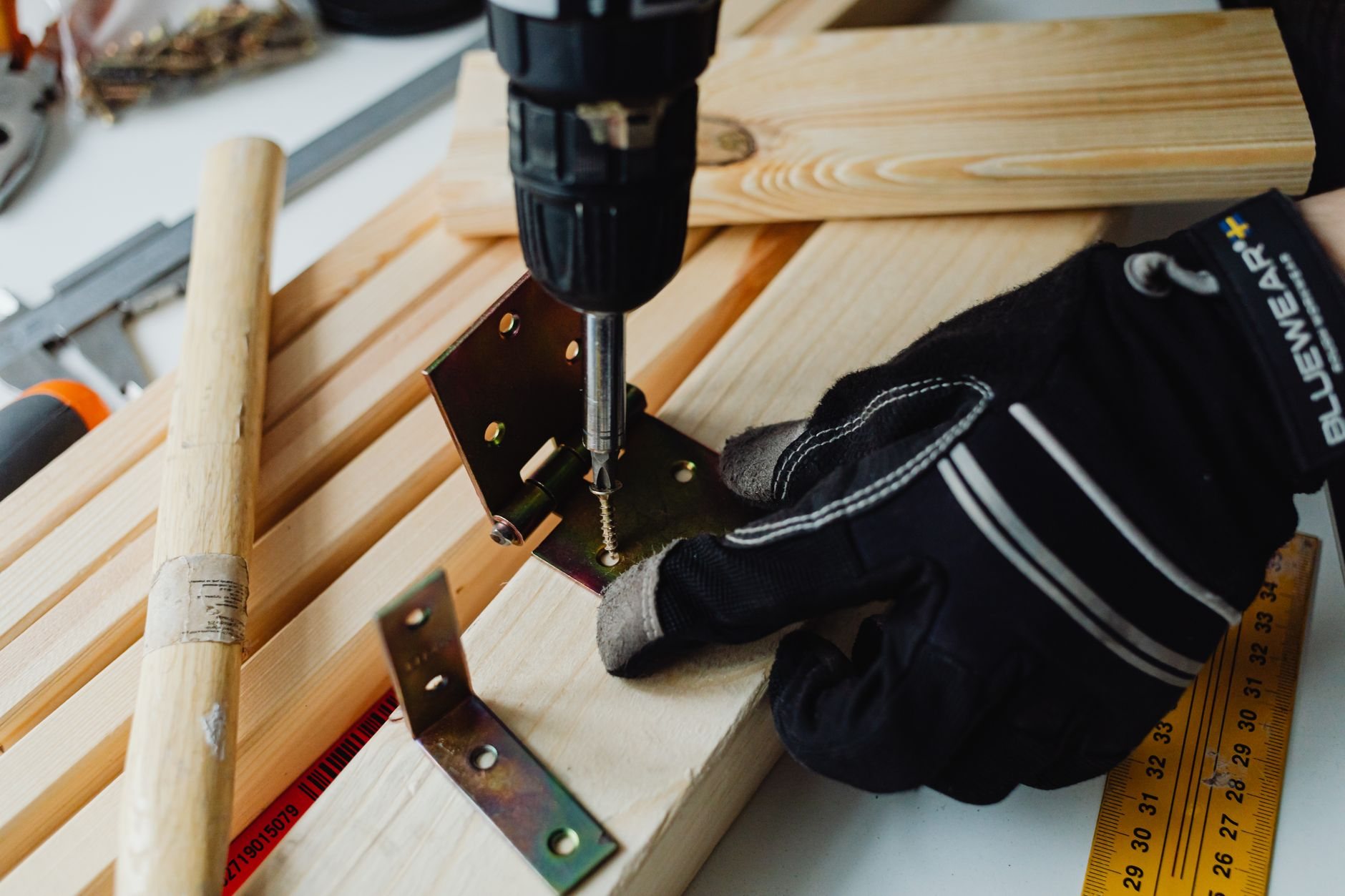 Finish carpentry in progress with a power drill, bracket, and safety gloves on a woodworking bench