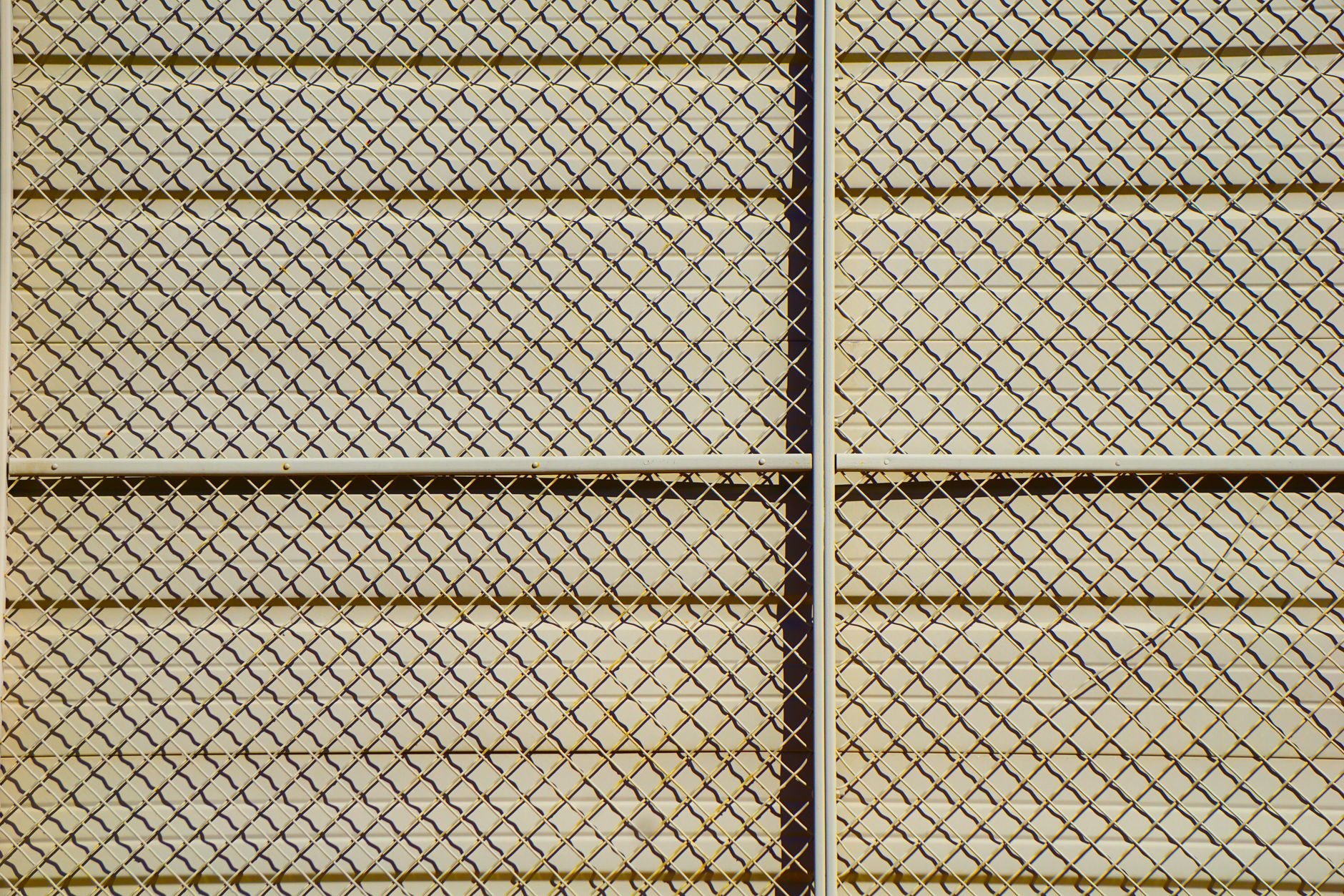 Chain-link fence fabric in afternoon light, showing the mesh pattern of a galvanized perimeter fence