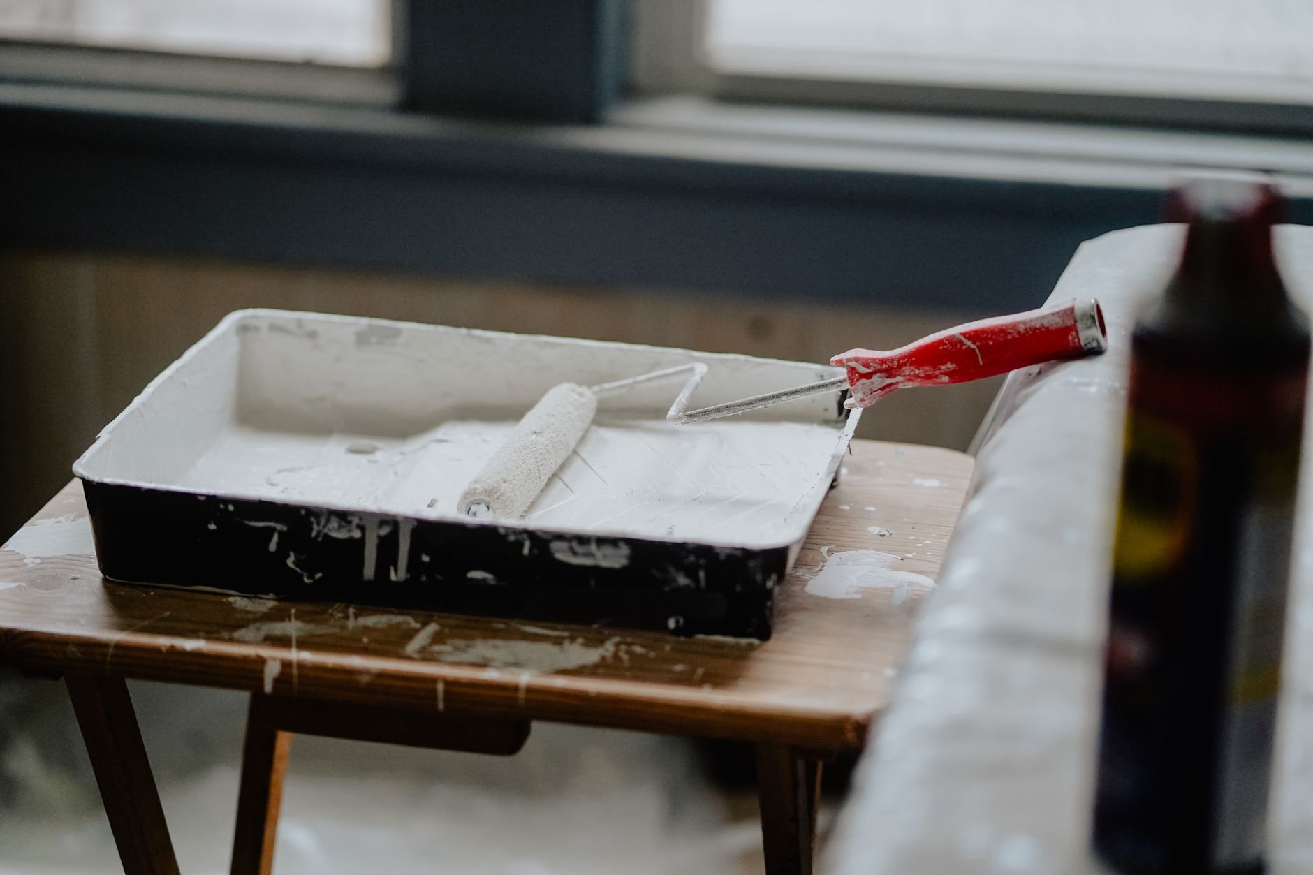 Paint roller and tray of white paint staged on a work table before an interior repaint