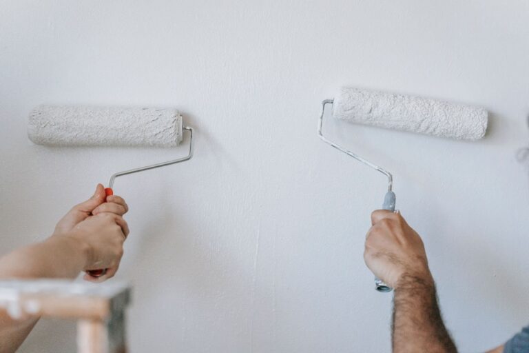 Paint and drywall work: close-up of two individuals painting a wall with paint rollers indoors