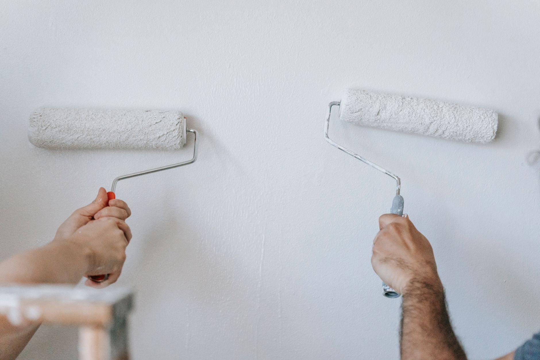 Two finishers working a freshly taped drywall wall with rollers during an interior renovation