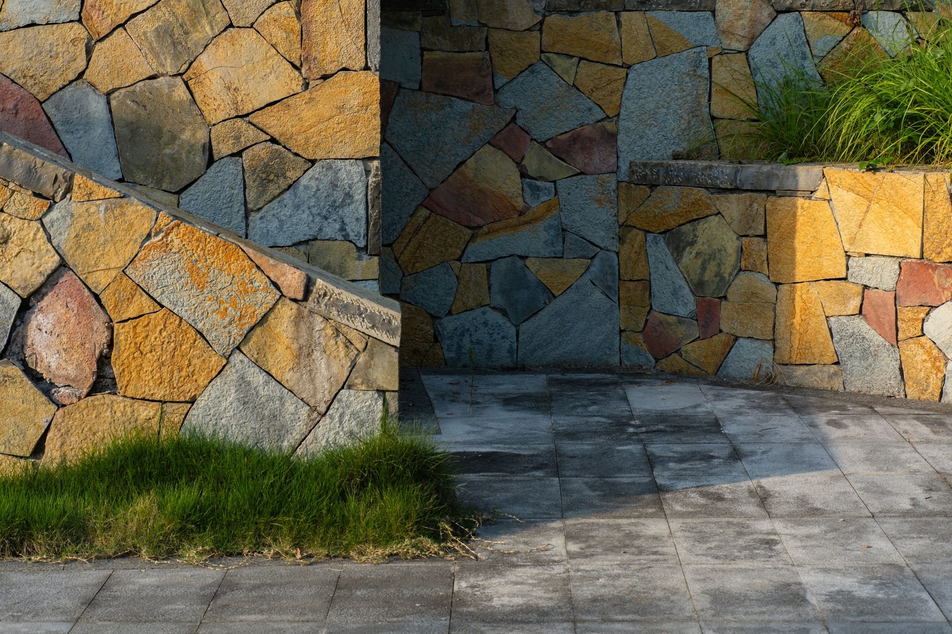 Stone retaining wall with paved ground and lawn on a sloped residential lot