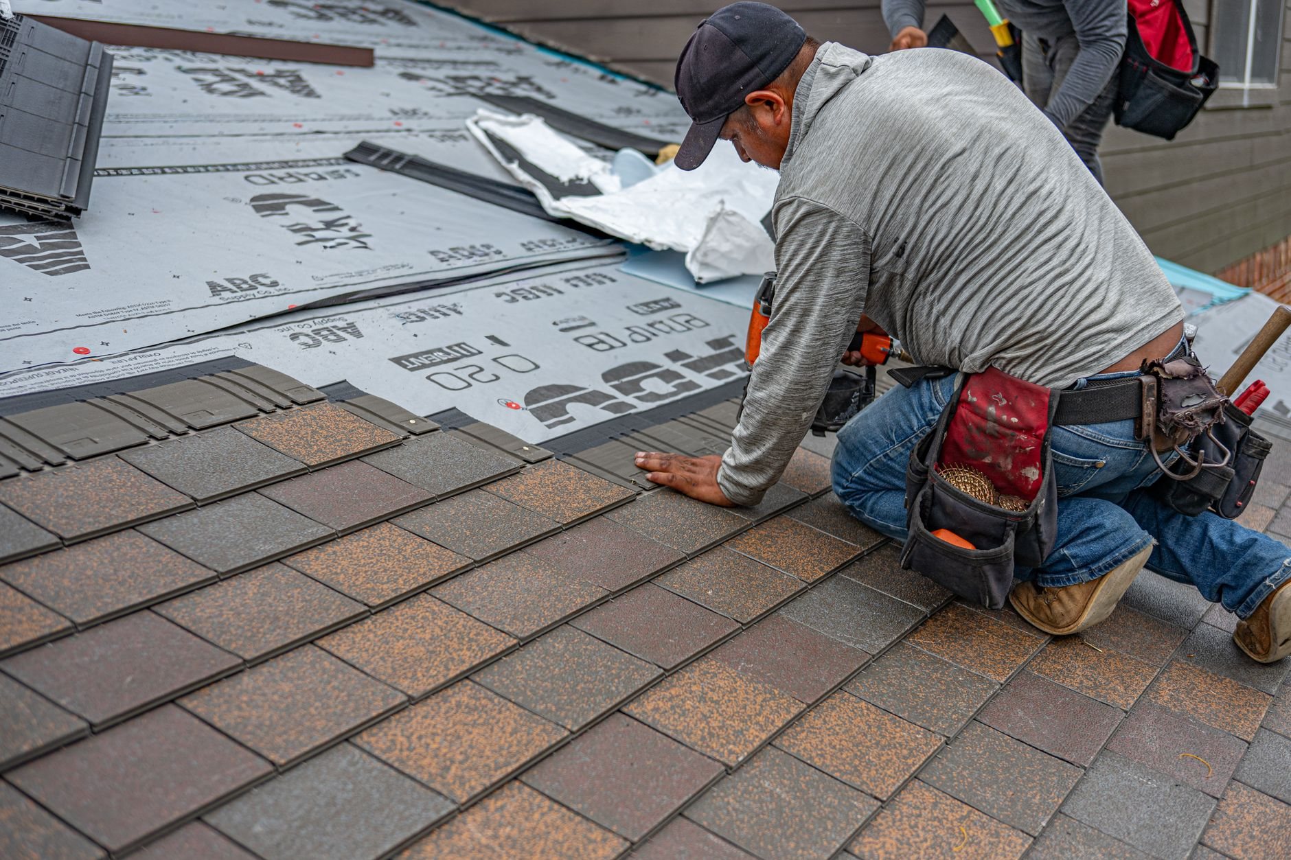 Roofer working at the eave line of an asphalt shingle roof where the gutter system attaches