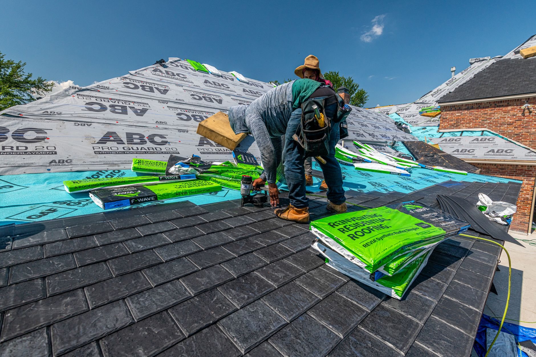 Roofing crew installing a synthetic slate roofing system on a brick home