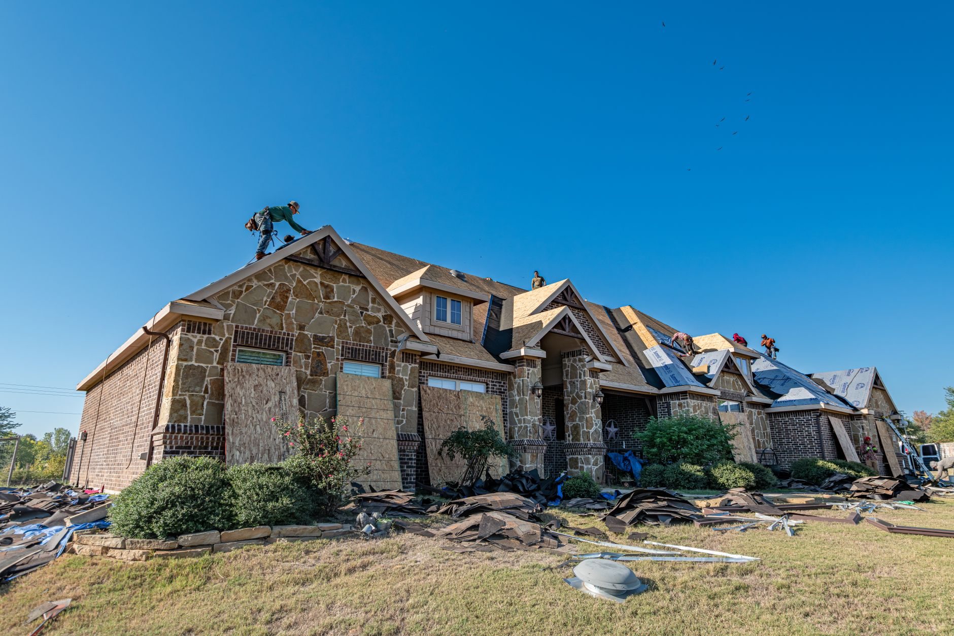 Roofing crew installing a new roof on a brick home under a clear sky