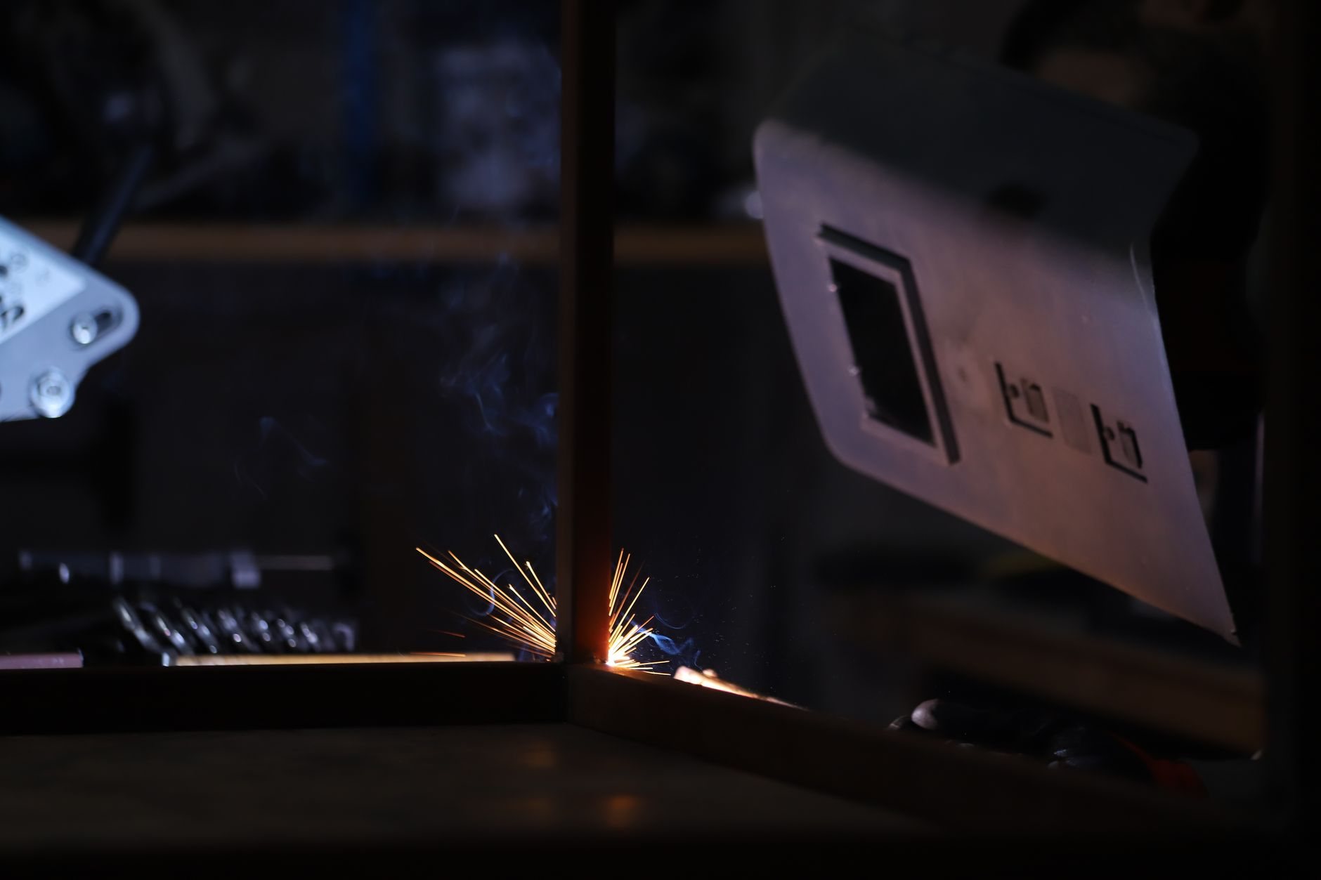 Welder laying a structural weld in a dark fabrication shop, bright sparks and protective gear visible